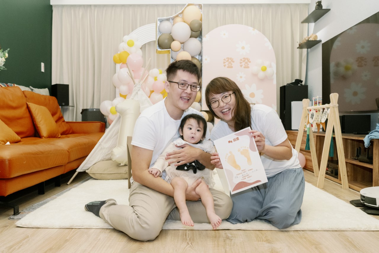 寶寶和爸媽坐在粉色背景牆前和腳印證書合照