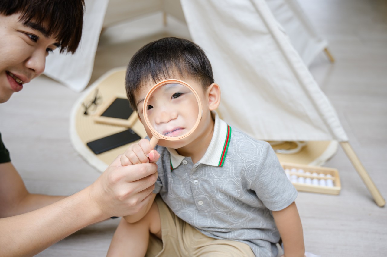 小男孩透過放大鏡看鏡頭