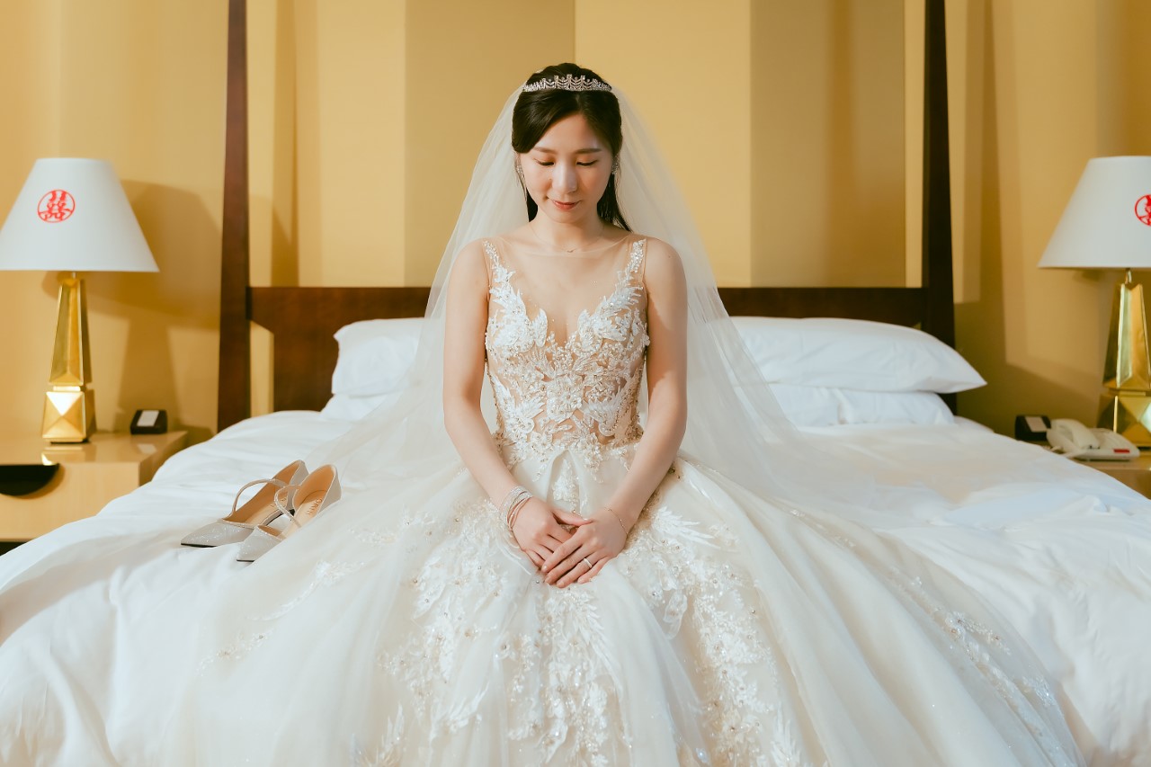 新娘身穿白紗低頭坐在床沿