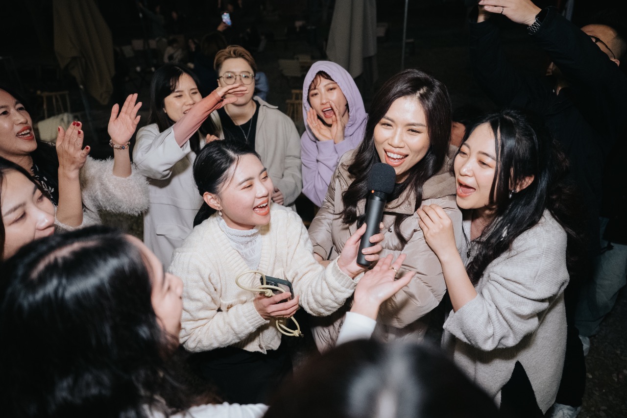 姊妹團在派對中圍成一圈開心合唱，拿著麥克風互動，展現真摯友情與婚禮的歡樂高潮